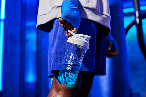 A person dressed in blue holds a bottle, focusing on the bottle's details, highlighting an emphasis on the carry loop and blue BlenderBall color.