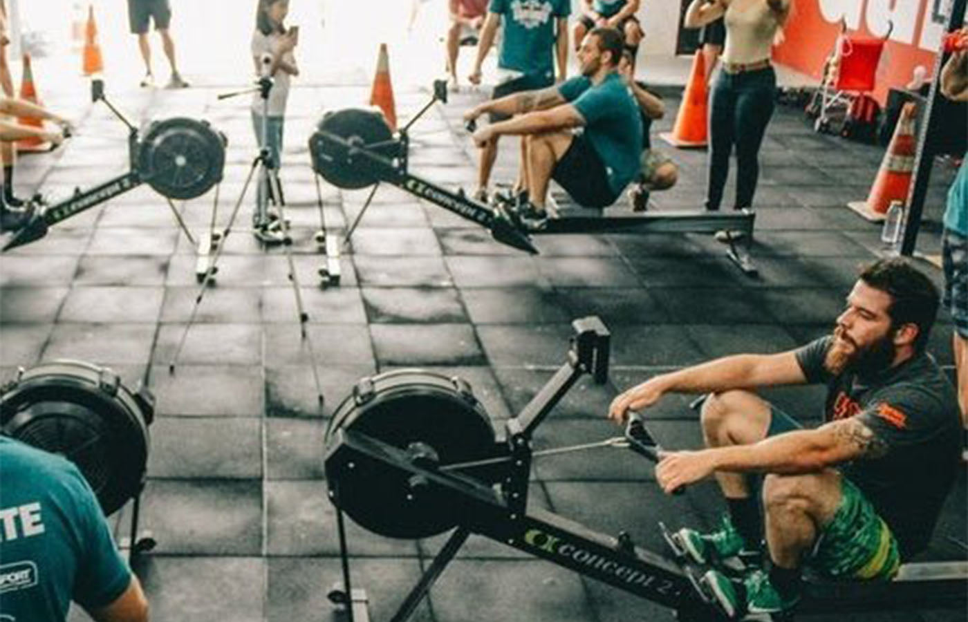 A group of people exercising in a gym with various equipment, featuring several men using machines.