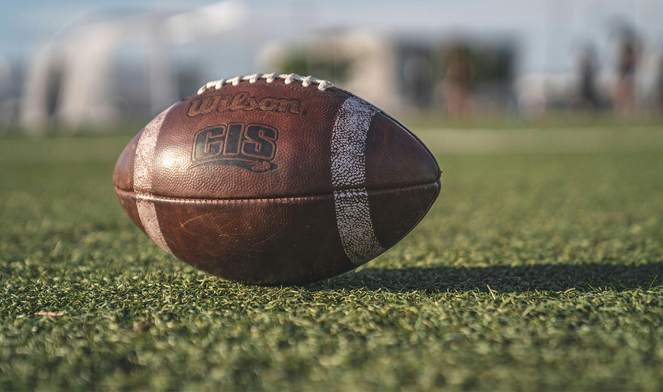 Close-up of a football resting on grass, highlighting its texture and stitching, set on an outdoor sports field.
