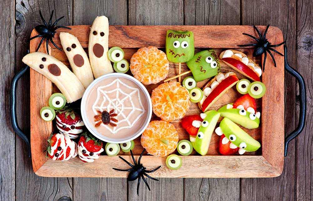 A tray featuring fruit and Halloween-themed treats, including a banana shaped like a ghost and peeled oranges with stems, resembling pumpkins.