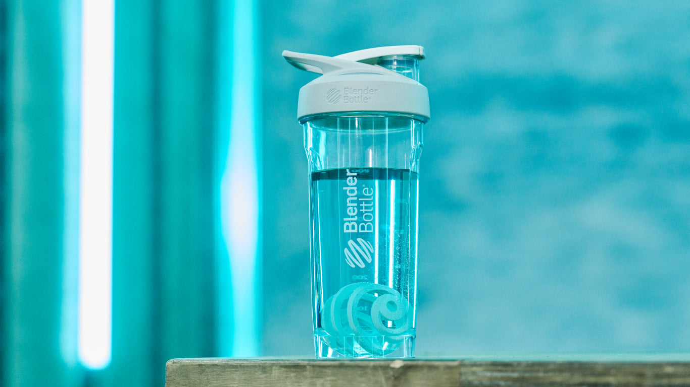 A clear BlenderBottle with a white lid on a wooden surface, with a blue BlenderBall color inside, emphasizing the bottle's sleek design and functionality.
