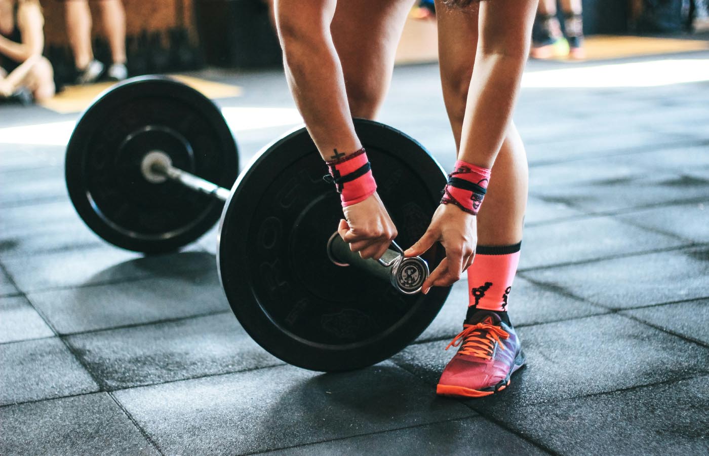 A person lifting weights in a gym, focusing on their hand gripping a barbell, with visible footwear and wristband.