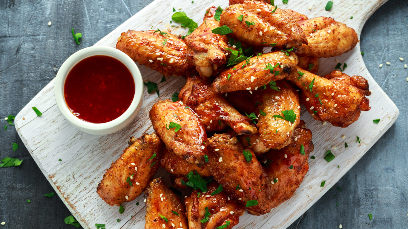 A plate of chicken wings garnished with parsley and sesame seeds, accompanied by a bowl of red sauce.
