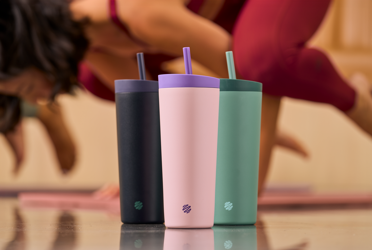 A collection of colorful BlenderBottle 2-in-1 Shaker Tumblers with straws displayed indoors, highlighting their vibrant designs and practical features.