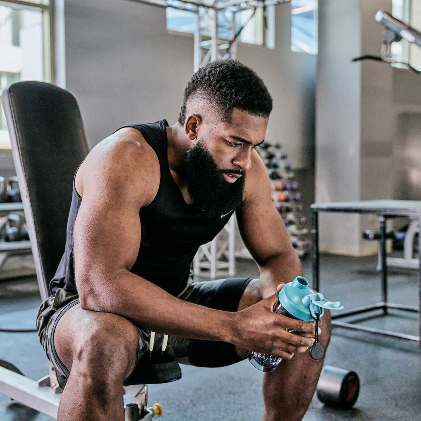 A man on a gym bench holding a blue BlenderBottle