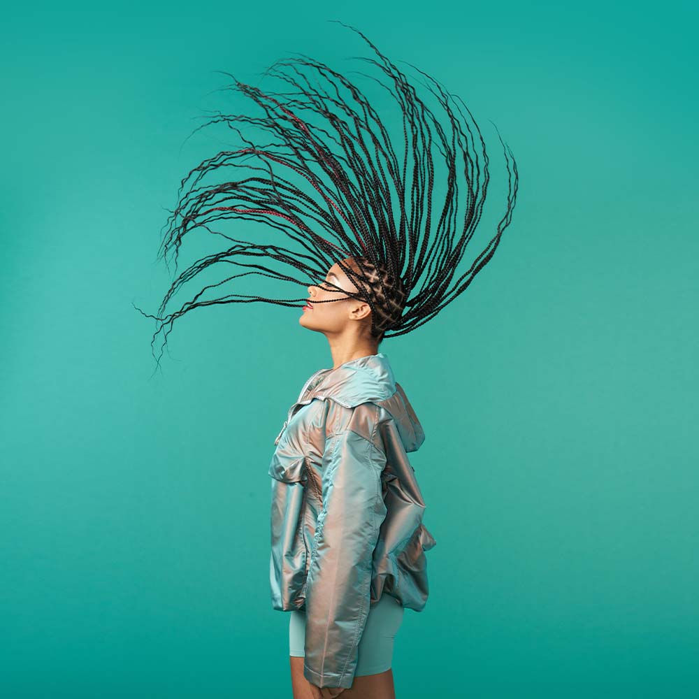 A woman dressed in an Ariel costume flipping her long hair. She is smiling and appears to be enjoying the moment. Her costume includes a green sequined top. The woman's pose and expression capture the playful and carefree spirit of the iconic Disney character.