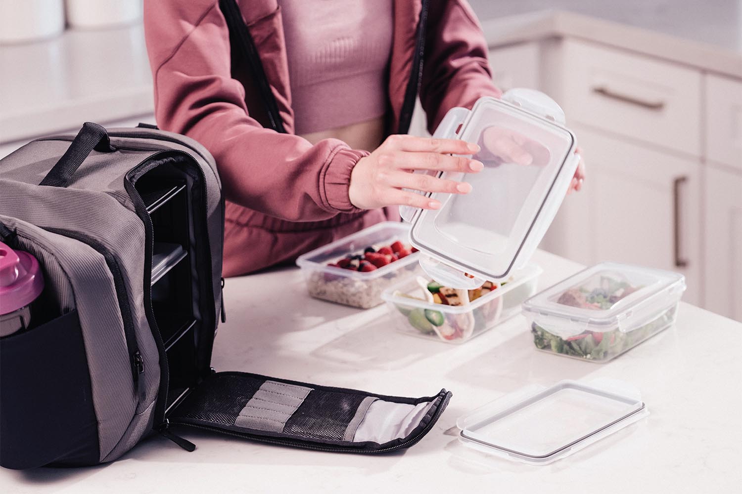 Woman packing a meal prep bag. Three meal containers are on the table ready to pack into the bag.