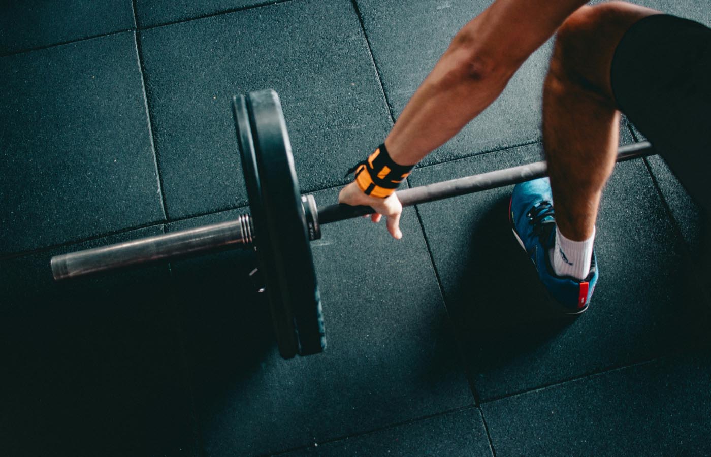 A person performing a barbell lift, showcasing strength training in a gym setting, with focus on their form and athletic footwear.
