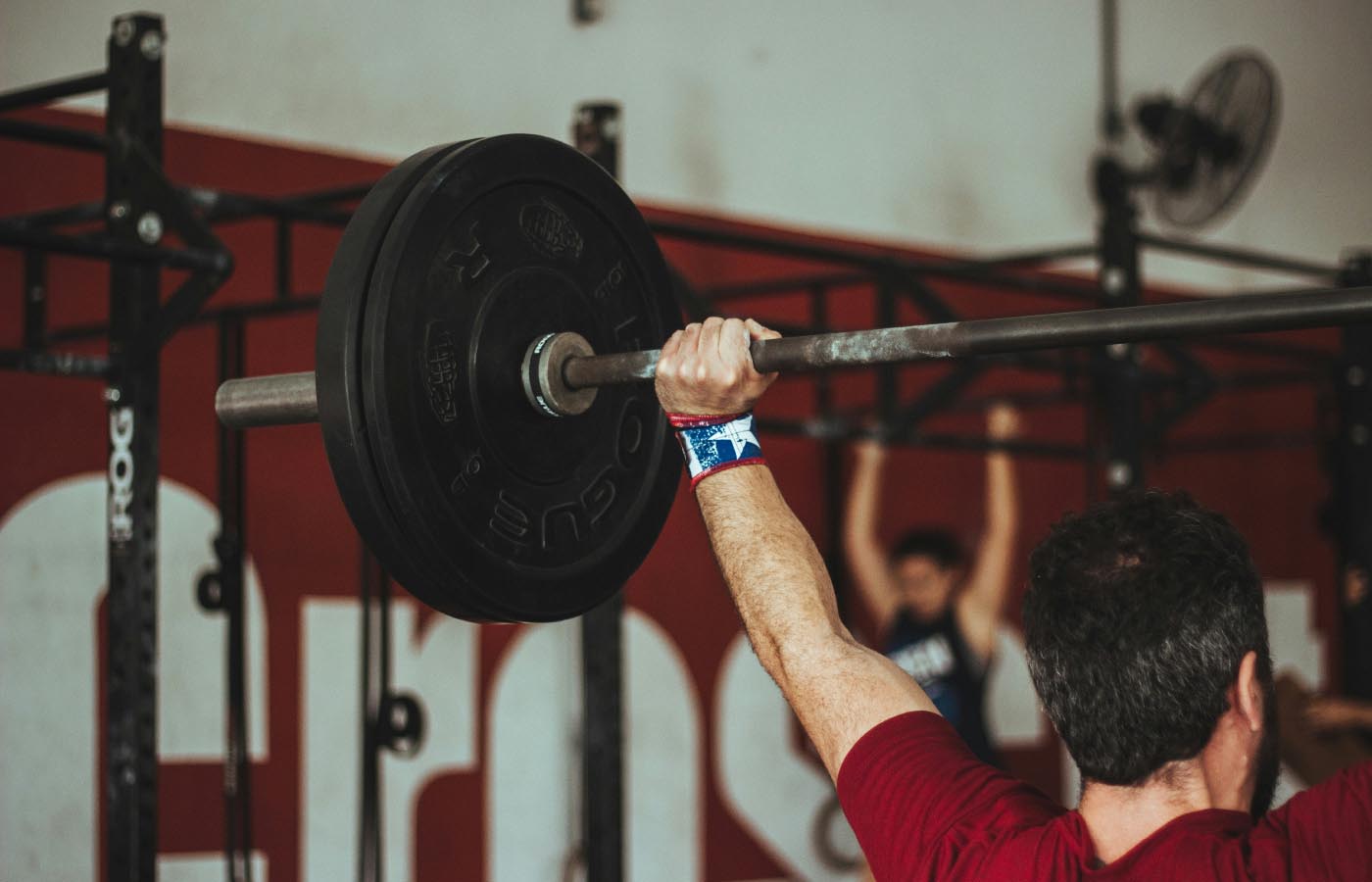 A man lifting a barbell in a gym setting, showcasing strength training with visible focus on weightlifting and physical fitness equipment.