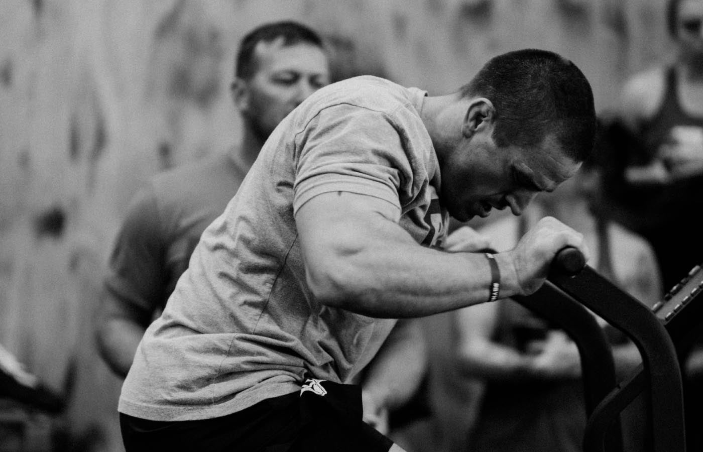 A man working out on a machine, with a focus on his arm muscles. The scene suggests an intense workout session.