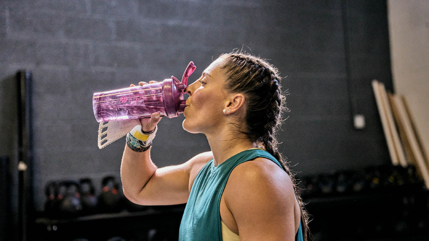 A woman drinks from a purple BlenderBottle in a close-up shot, suggesting a health or fitness context.