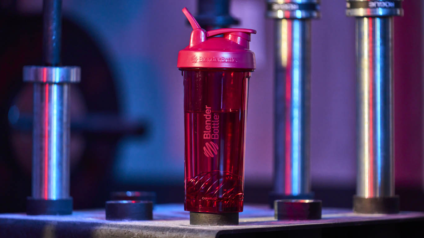 Close-up of a red blender bottle with a matching red lid, set on a table. 