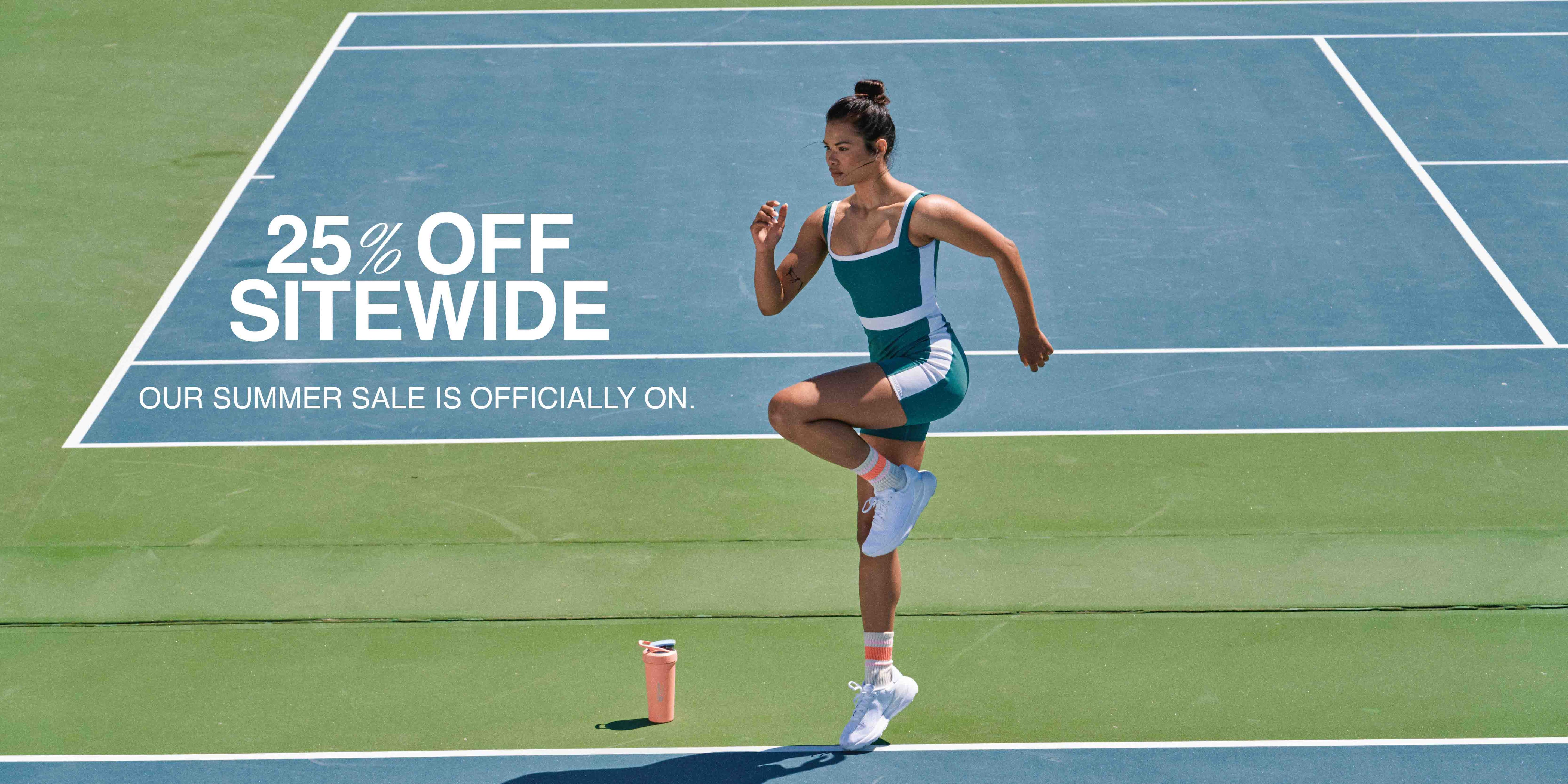 A woman in a blue and white tennis outfit stands on a tennis court, wearing athletic shoes, warming up to play.