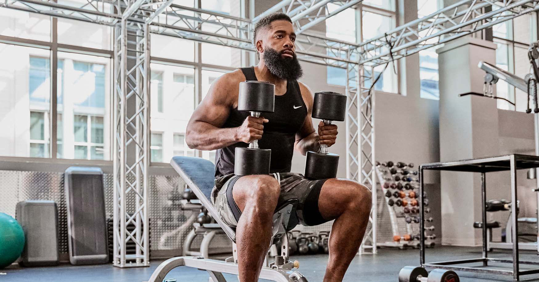 Man lifting dumbbells seated on gym bench press, engaging chest and arm muscles. Knurled metal handle dumbbells and sturdy padded bench.