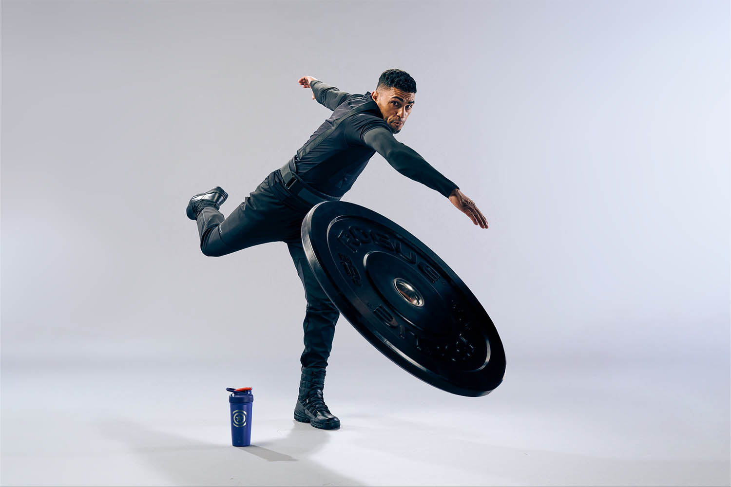Man dressed as Captain America throwing a 10lb plate with a Captain America insulated stainless steel protein shaker cup at his feet