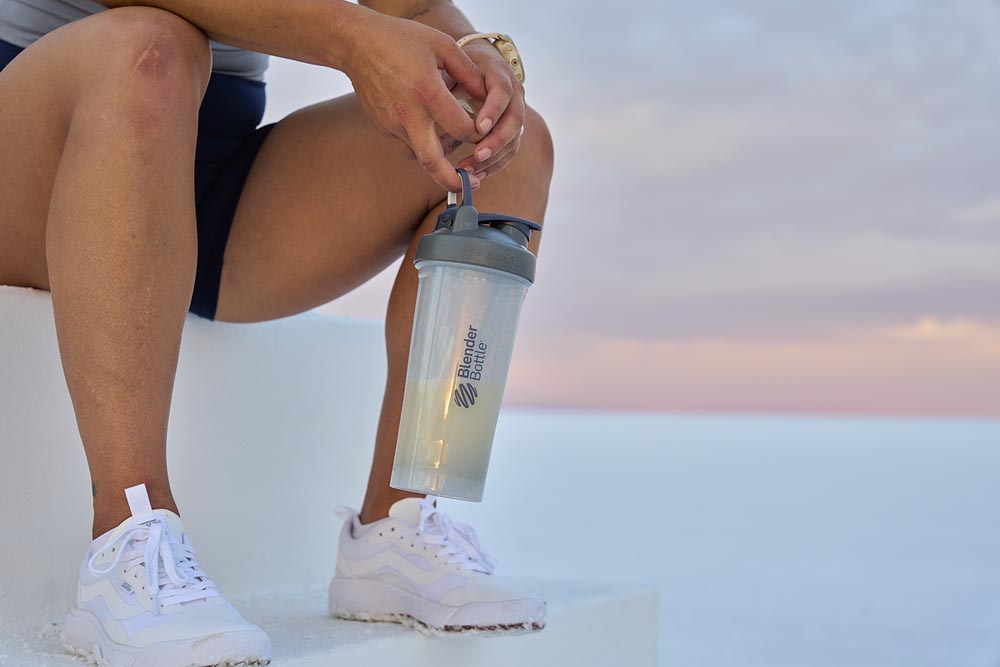 Woman holding a grey protein shake cup.