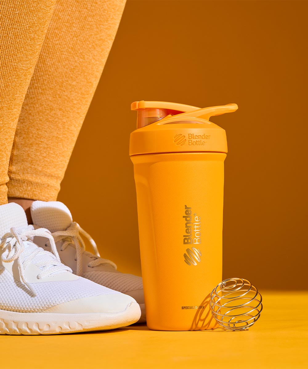 A yellow double wall insulated stainless steel shaker cup at the feet of a woman working out.