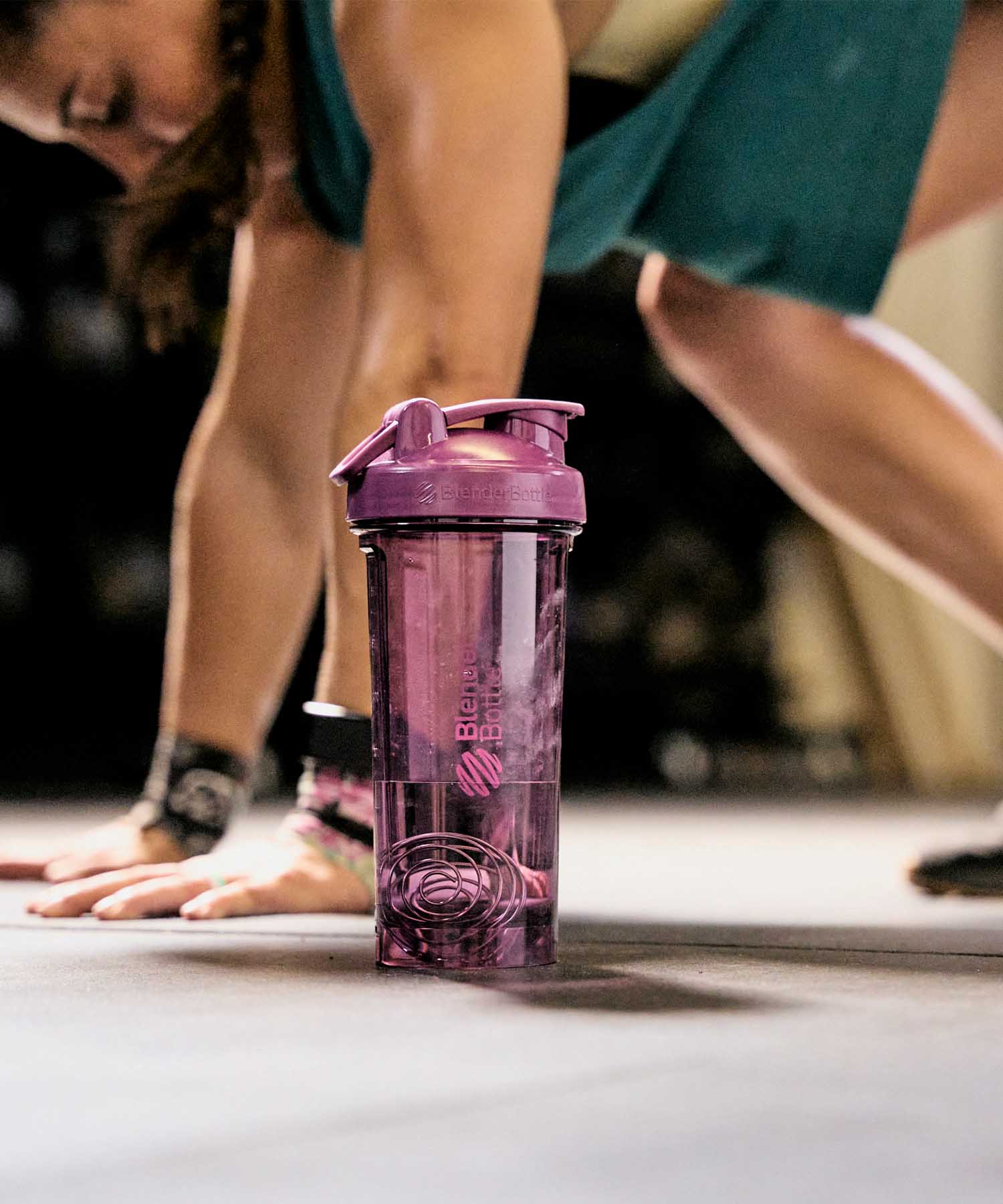 A Pro Series premium shaker bottle on the ground while a woman works out in the background