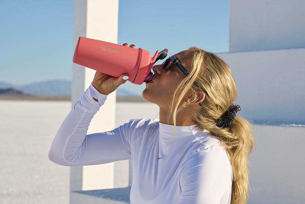 Woman drinking from Strada Trian stainless steel shaker bottle.