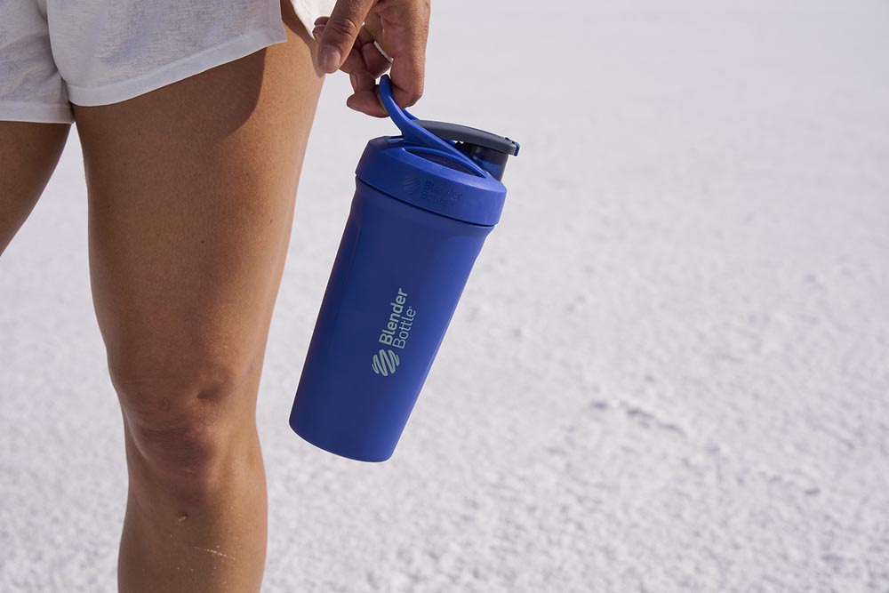Woman holding blue insulated stainless steel protein shake bottle.