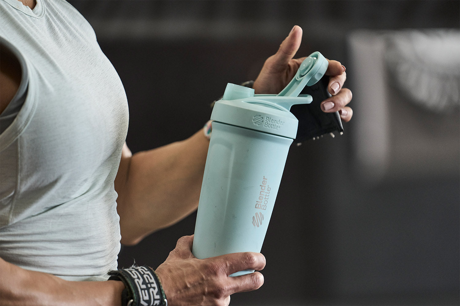 Woman using light blue shaker bottle with a twist lid in the gym